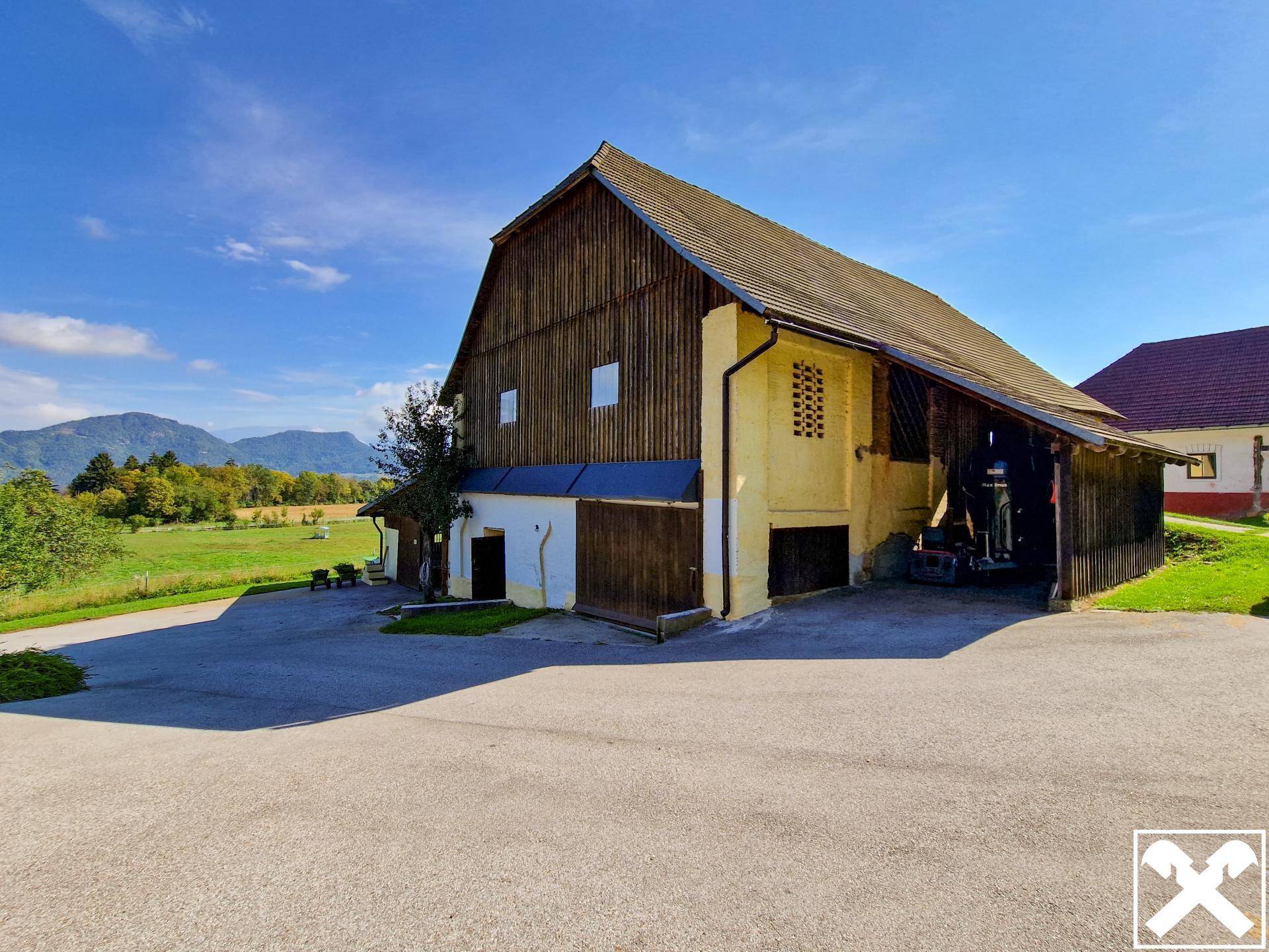 Traditionelles Bauernhaus mit Holzverkleidung und weitem Vorplatz unter blauem Himmel.