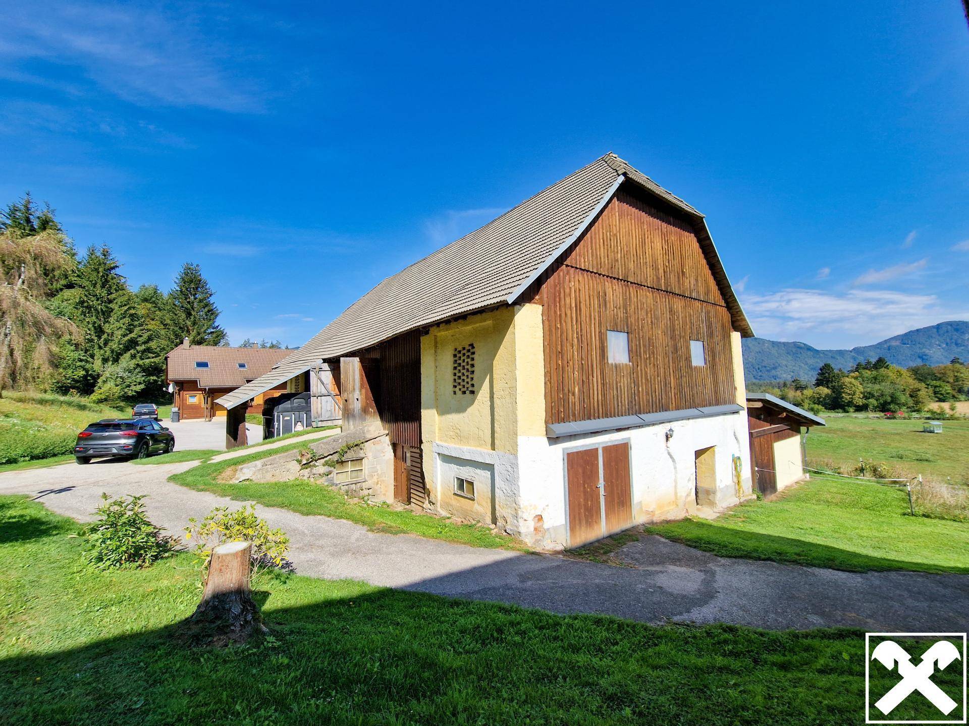 Großes Bauernhaus mit Holzfassade und angrenzendem Stallgebäude im Grünen.