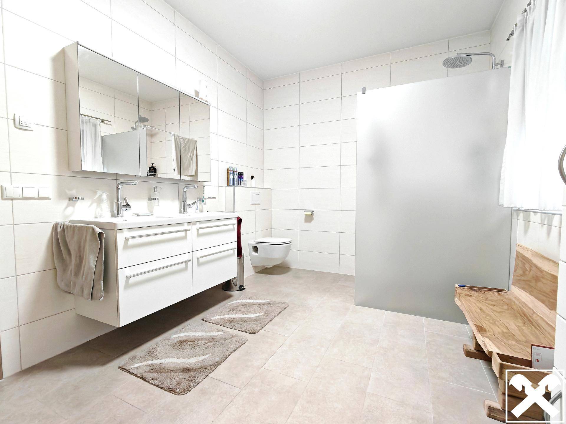 Geräumiges Badezimmer mit Doppelwaschbecken, großer Dusche und wandhängender Toilette.