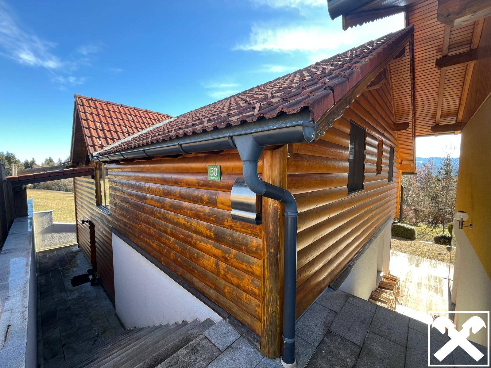 Detailansicht der Holzfassade und des roten Ziegeldachs mit Regenrinne und Hausnummer.