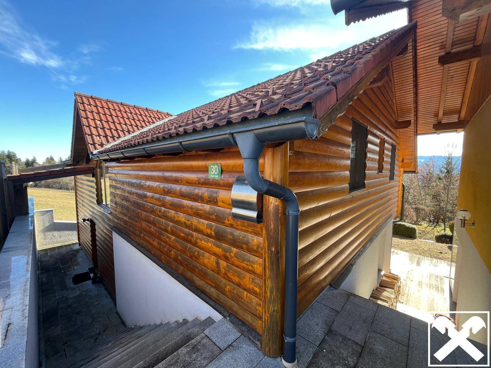 Detailansicht der Holzfassade und des roten Ziegeldachs mit Regenrinne und Hausnummer.