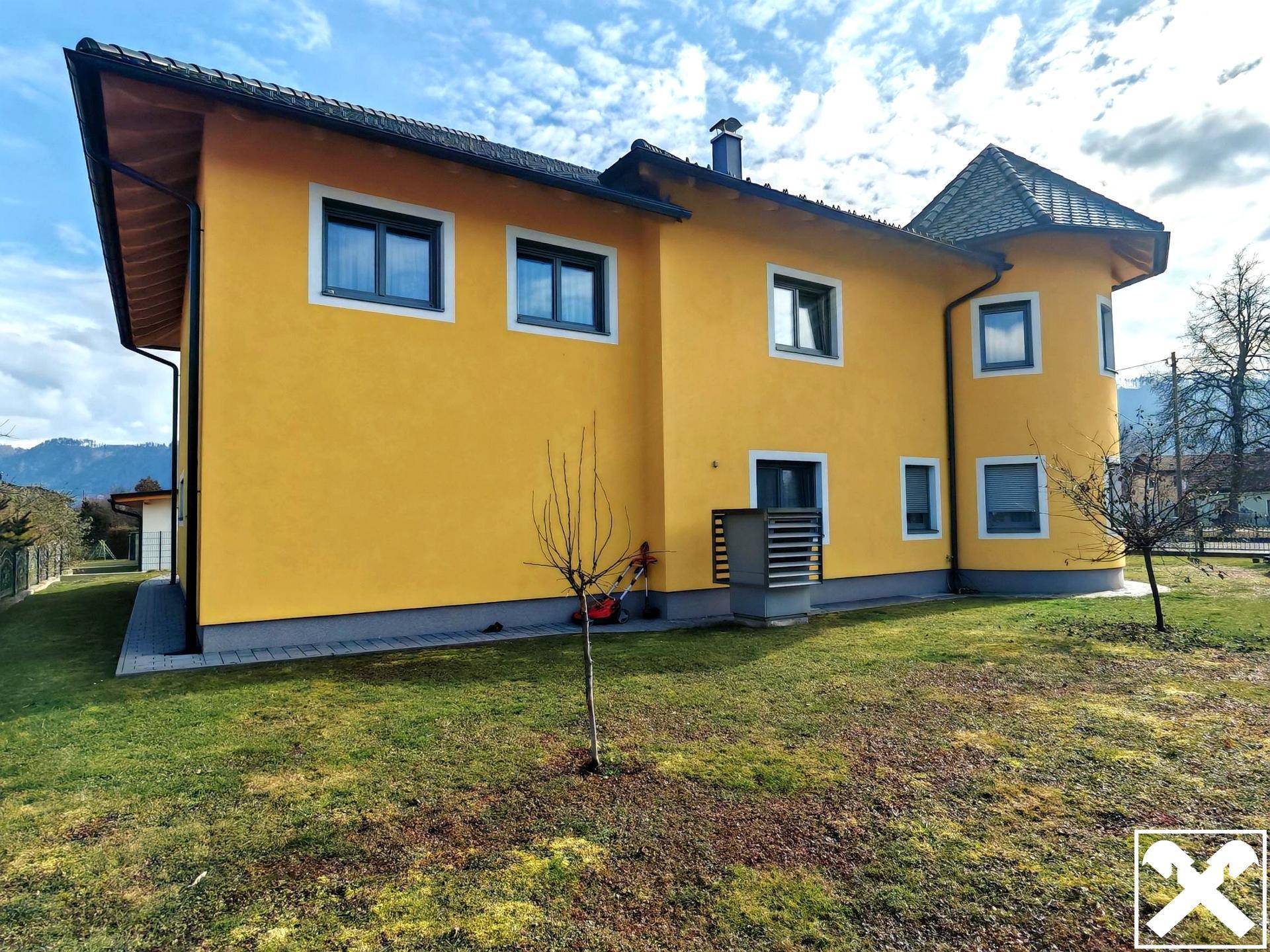 Seitenansicht des gelben Hauses mit Rasenfläche und Blick auf die Berge im Hintergrund.