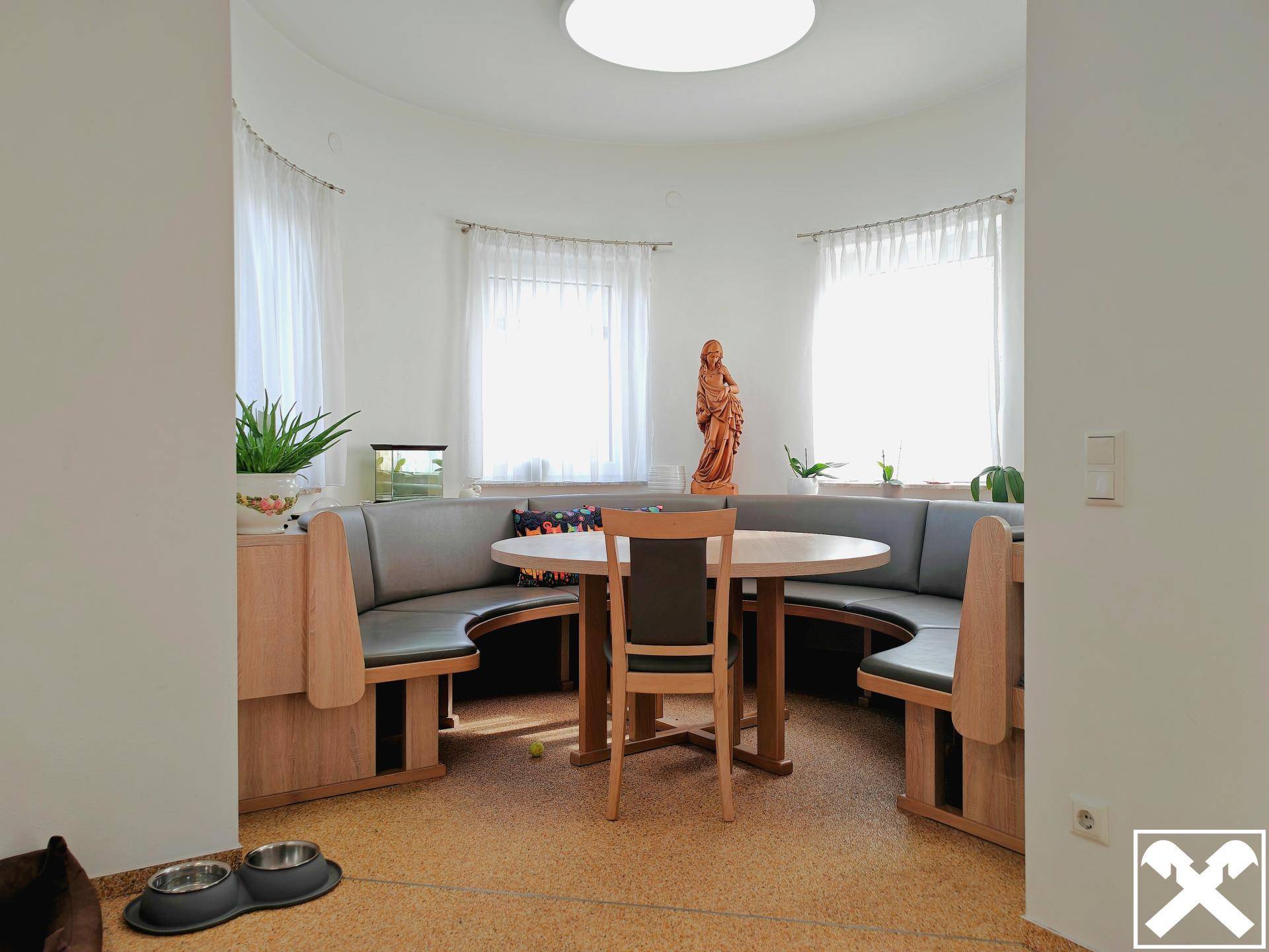 Heller Essbereich im Rundturm mit runder Sitzbank, Holztisch und mehreren Fenstern.