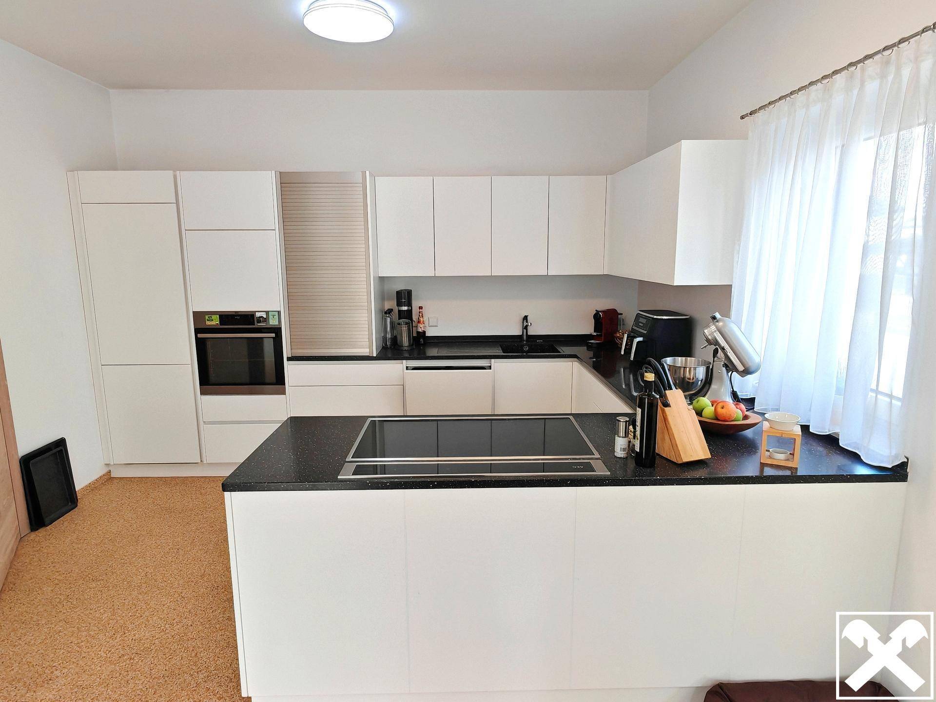 Moderne weiße Küche mit Kochinsel, schwarzen Arbeitsplatten und Induktionskochfeld.