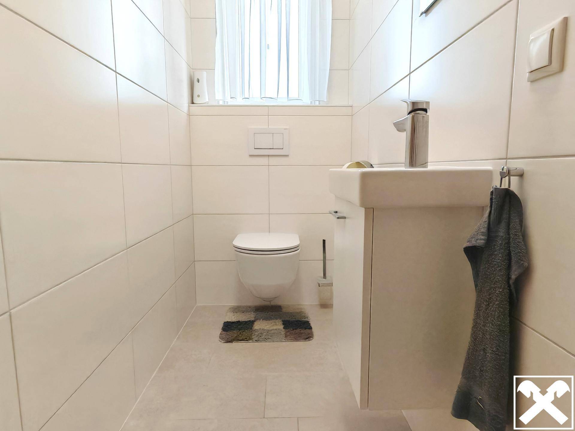 Helles Gäste-WC mit wandhängender Toilette, kleinem Waschbecken und Fenster.