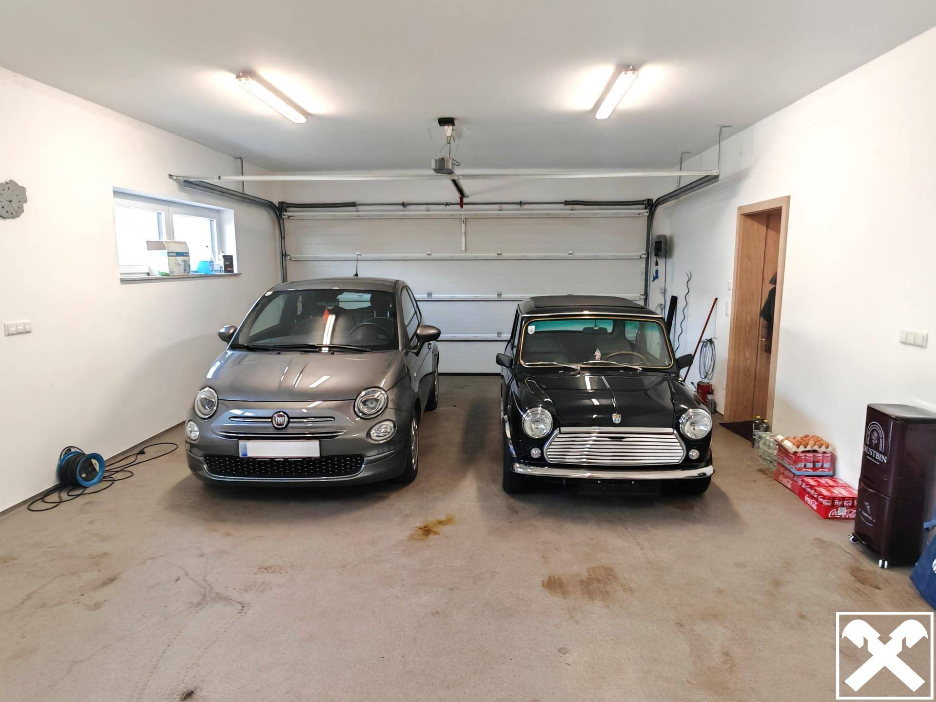 Garage mit zwei geparkten Autos, Garagentor und Fenstern für Tageslicht.