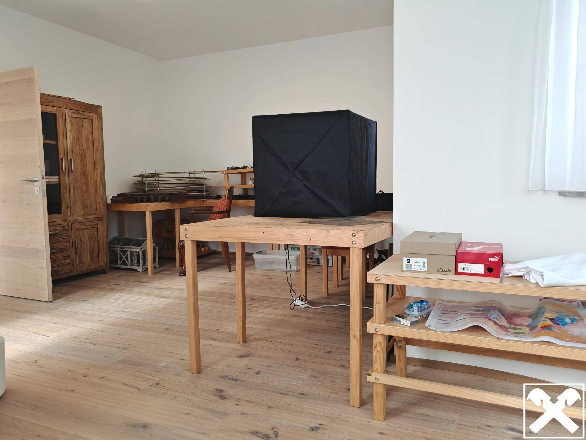 Heller Raum mit Holzboden, Holztischen und verschiedenen Gegenständen.