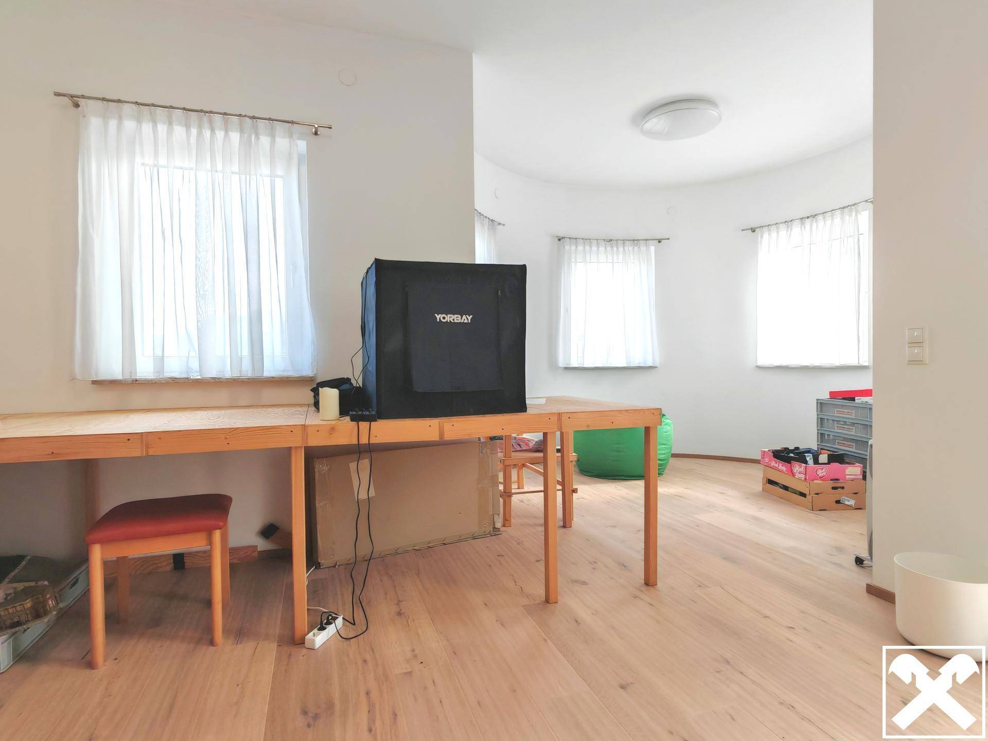 Heller Raum mit Holzboden, Schreibtisch und mehreren Fenstern.