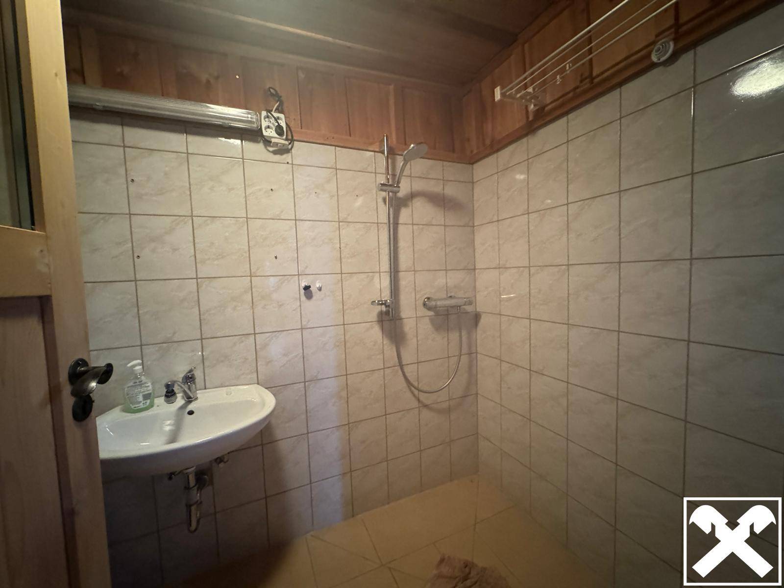 Einfaches Badezimmer mit gefliesten Wänden, Dusche und Waschbecken.