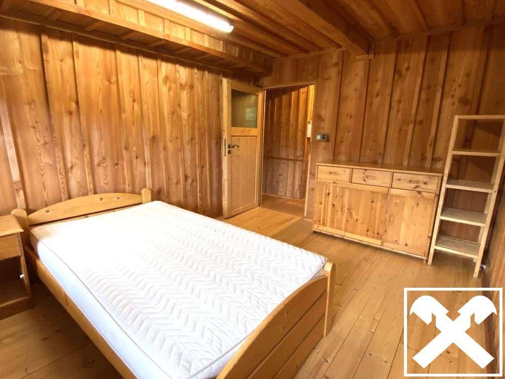 Schlafzimmer mit Holzboden und -wänden, ausgestattet mit Bett und Holzmöbeln.
