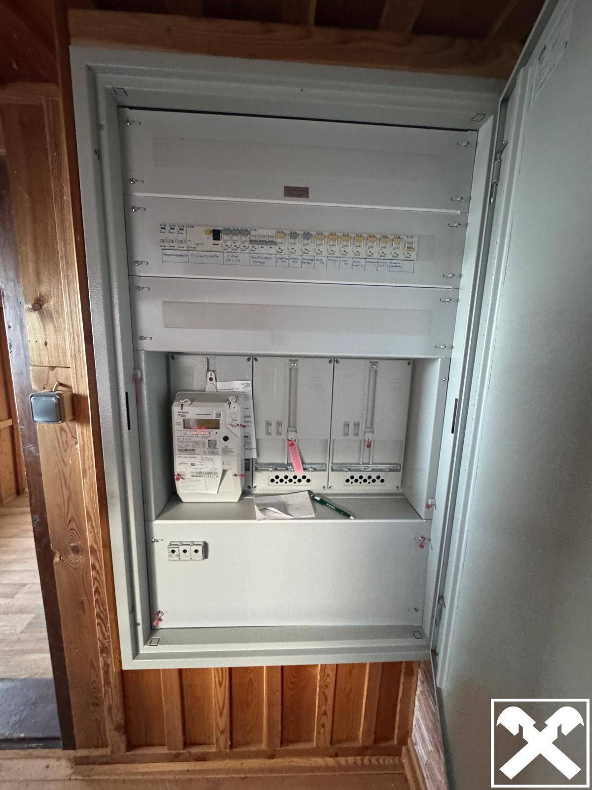 Elektrischer Verteilerkasten und Zähler in einem Raum mit Holzvertäfelung.