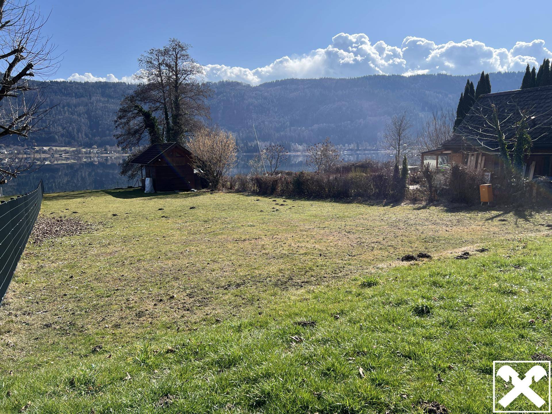 Große, sonnige Rasenfläche mit freiem Blick auf den See und die bewaldeten Berge.