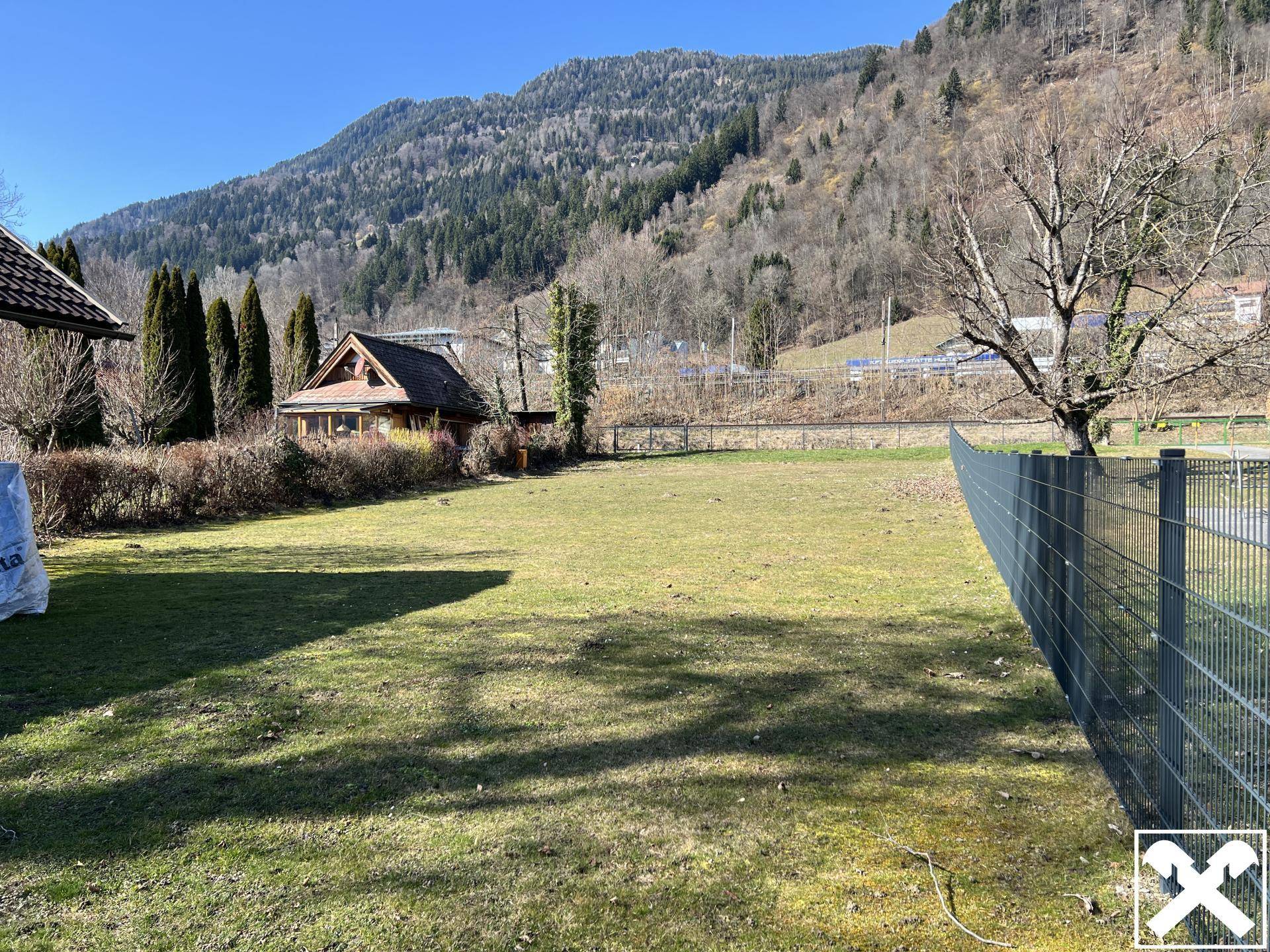 Gepflegte Rasenfläche mit kleinem Holzhaus und Blick auf die bewaldeten Berghänge.