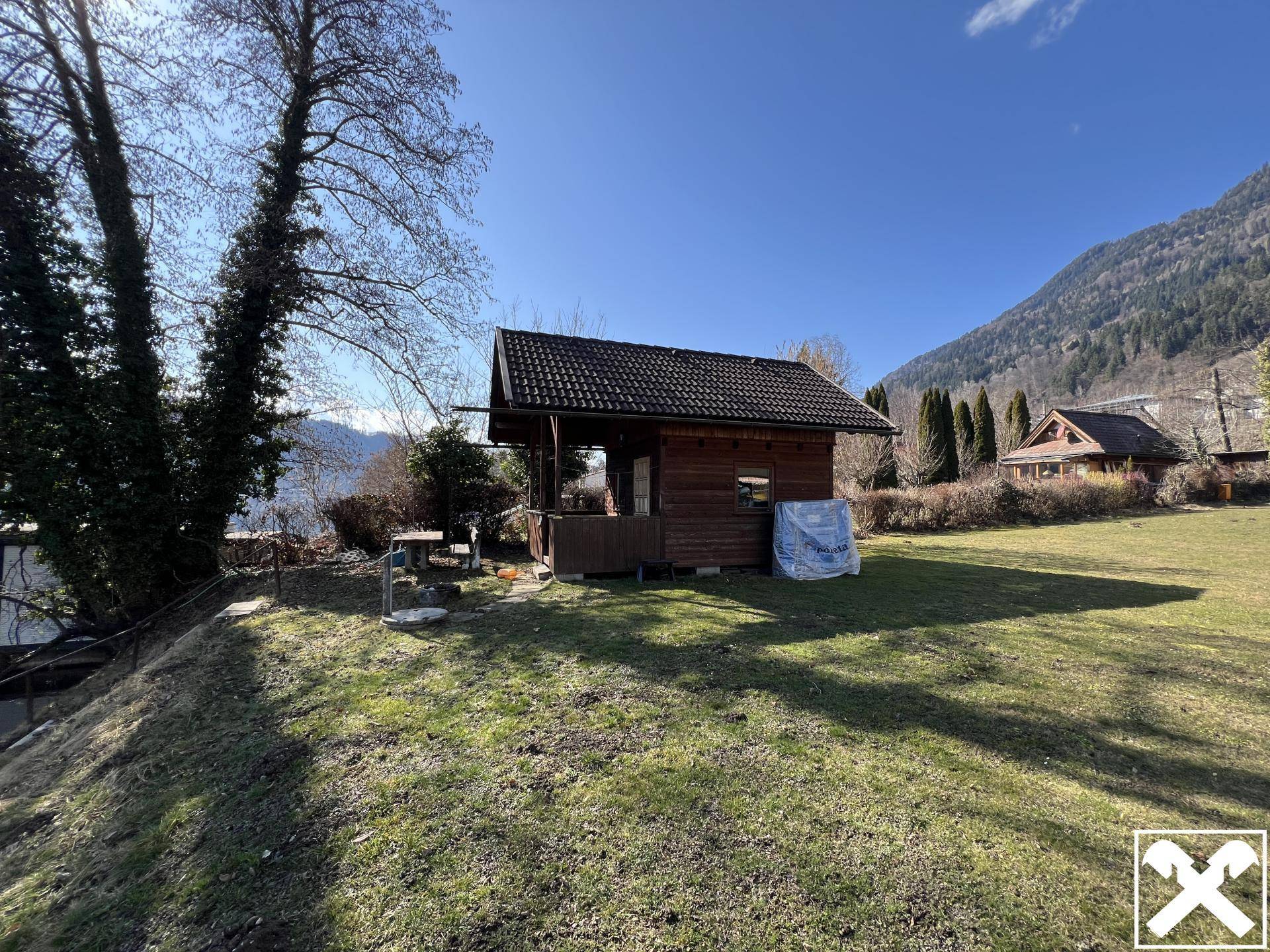 Kleines Holzhaus mit Veranda auf einer grünen Wiese mit See- und Bergblick.