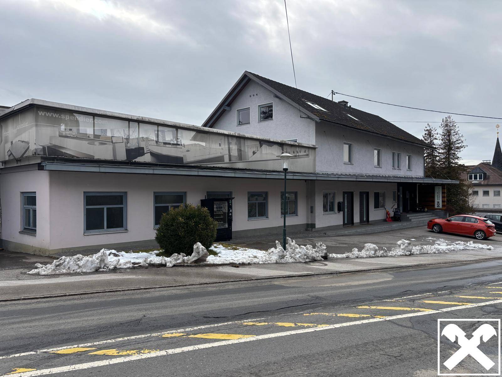 Gebäudeansicht mit einem kommerziellen Bereich im Erdgeschoss und Schnee am Straßenrand im Winter.