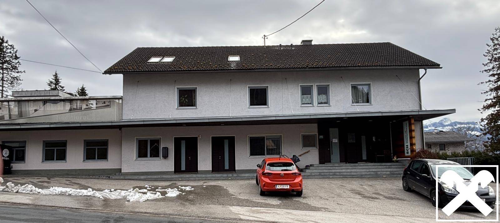 Vorderansicht des Gebäudes mit mehreren Eingängen und geparkten Autos auf dem Vorplatz im Winter.
