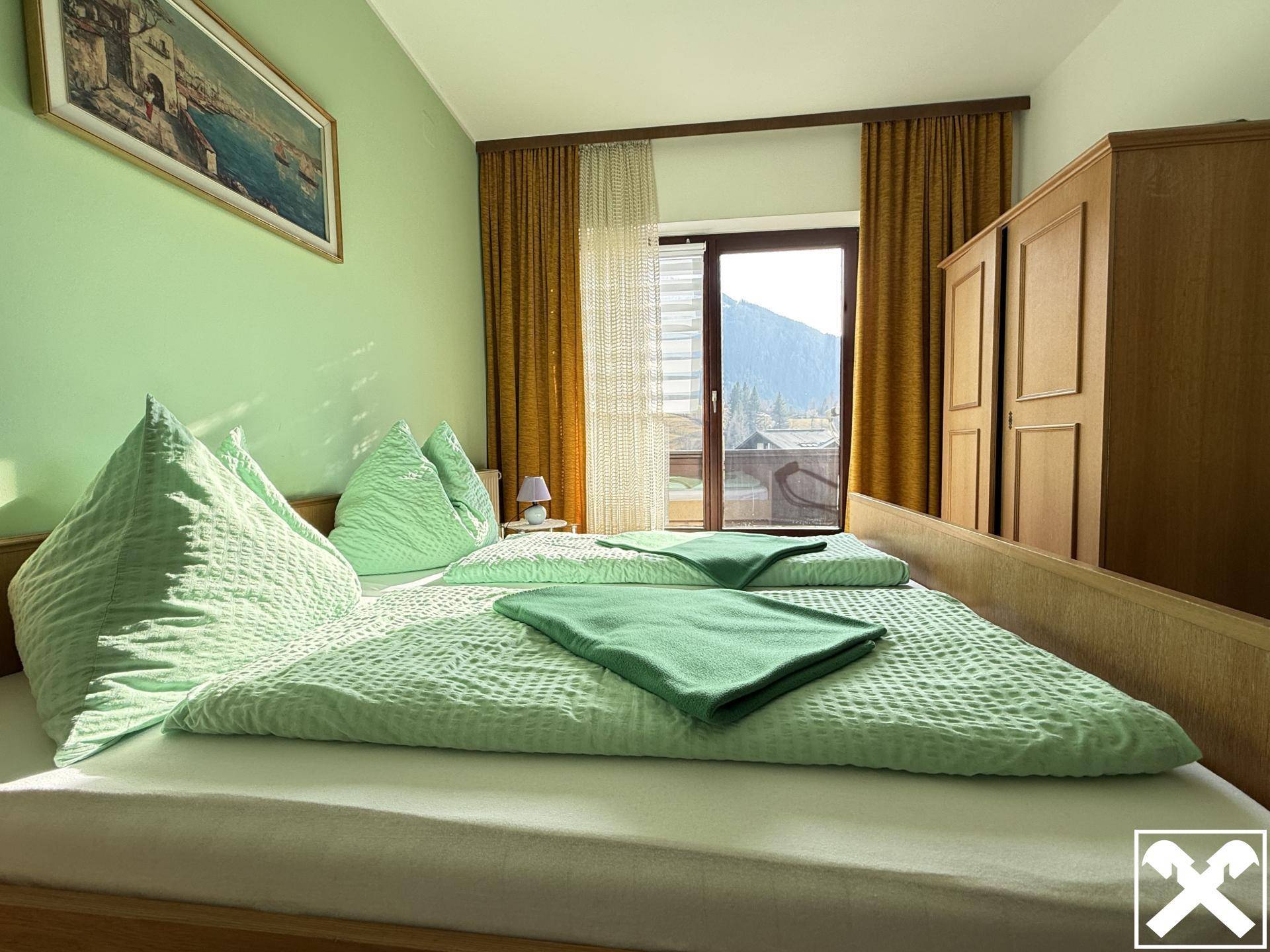 Schlafzimmer mit hellgrünen Wänden, Holzmöbeln und Zugang zu einem Balkon mit Bergblick.