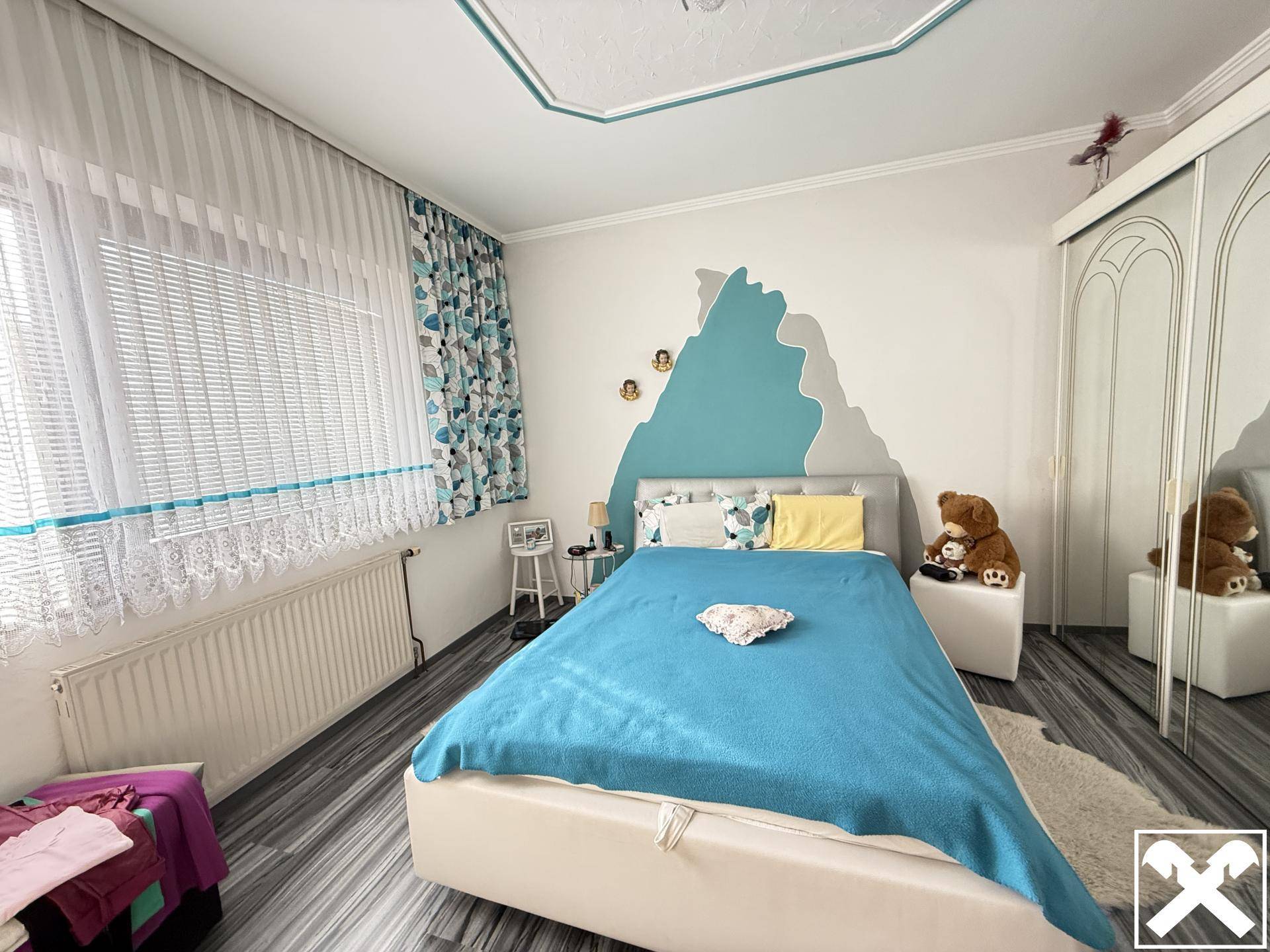Helles Schlafzimmer mit modernem Laminatboden, weißem Kleiderschrank und farbiger Wandgestaltung.