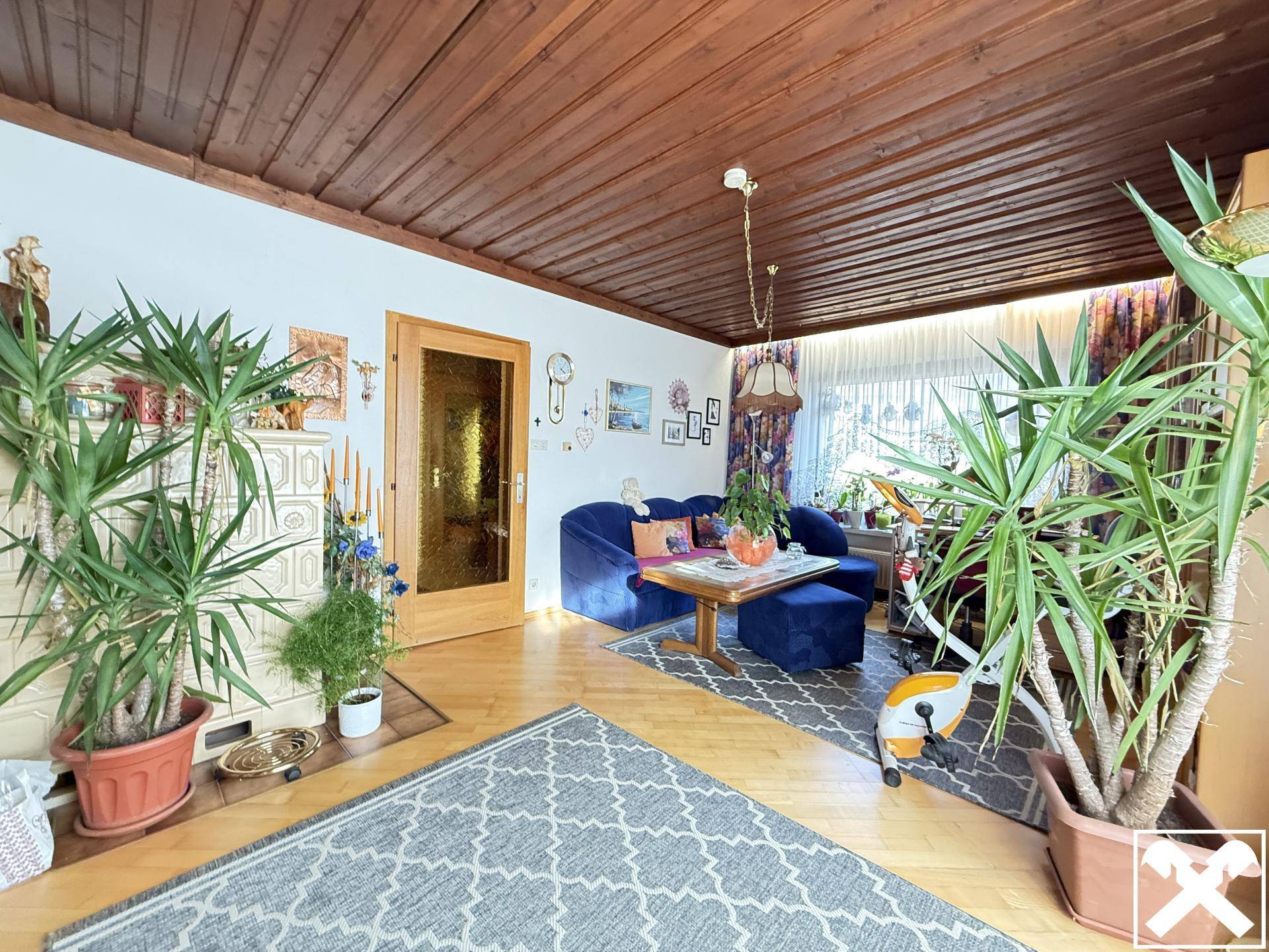 Gemütliches Wohnzimmer mit Holzbalkendecke, Parkettboden und vielen Grünpflanzen.