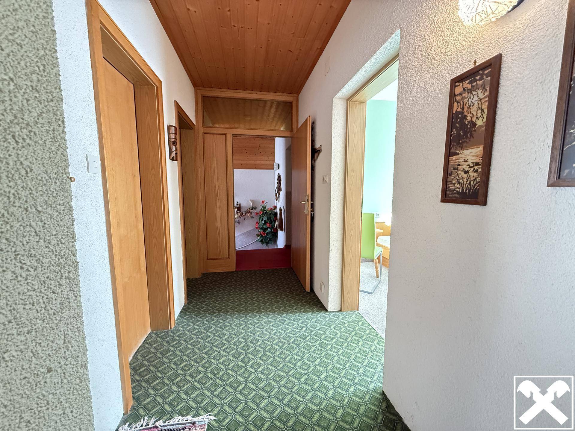 Flur mit gemustertem Teppichboden, Holzdecke und mehreren Türen zu angrenzenden Räumen.