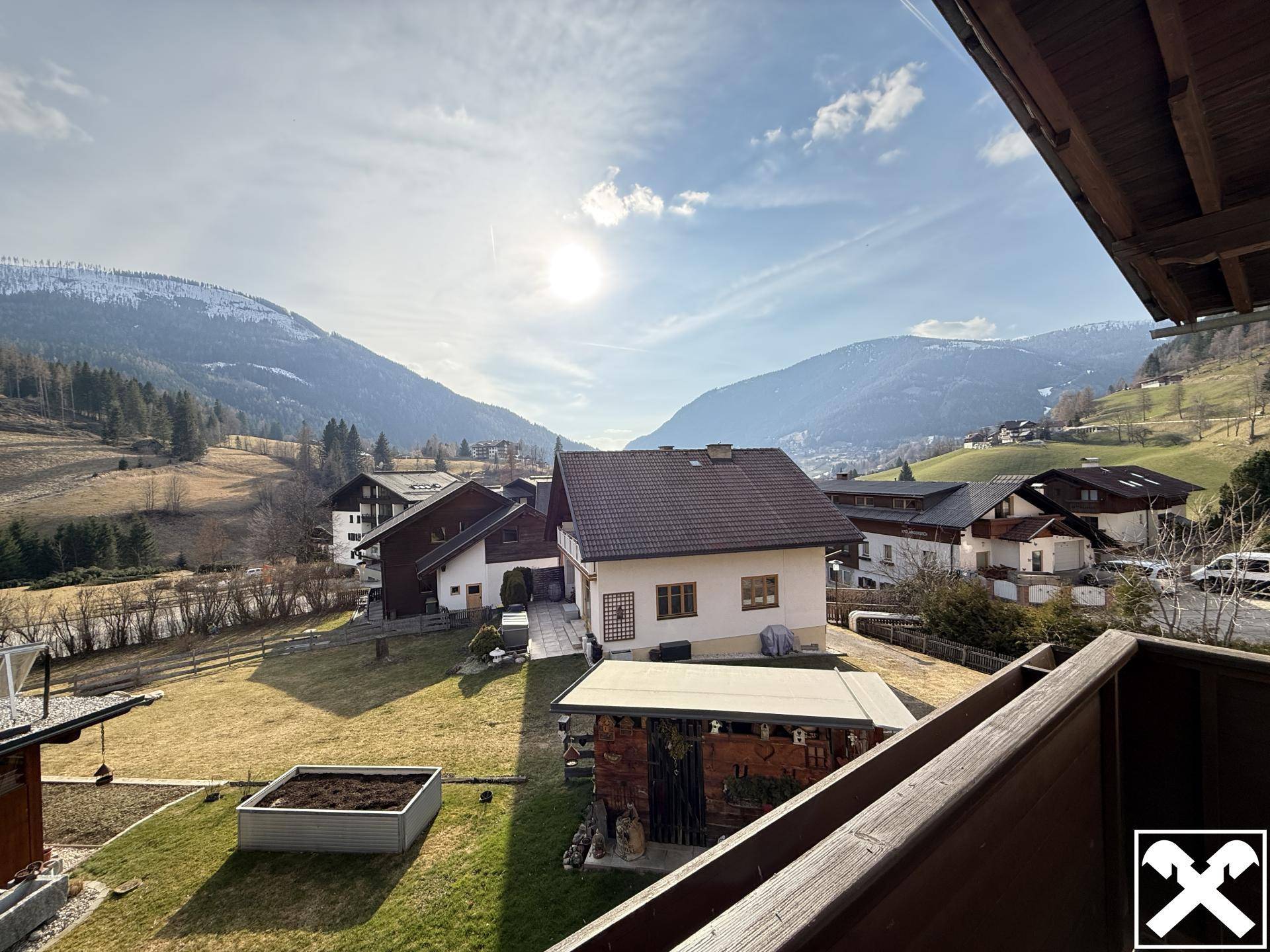 Weitläufiger Blick über eine alpine Landschaft mit Häusern und schneebedeckten Bergen.