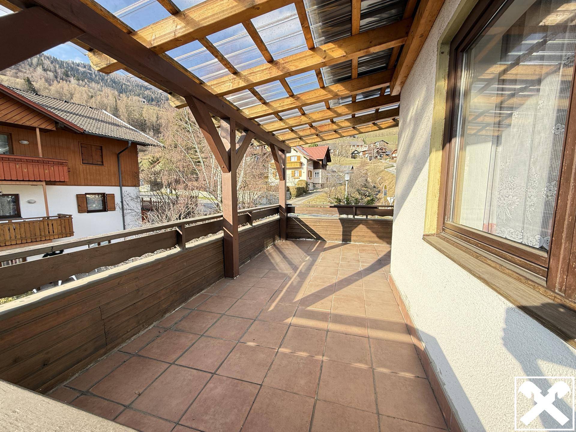 Geräumiger Balkon mit Holzdach, Fliesenboden und weitem Blick auf die umliegende Landschaft.