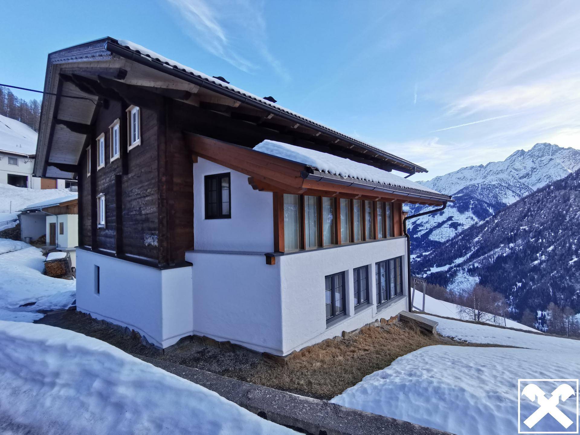 Seitenansicht des Holzchalets im Schnee, eingebettet in eine malerische Berglandschaft mit weitem Ausblick.