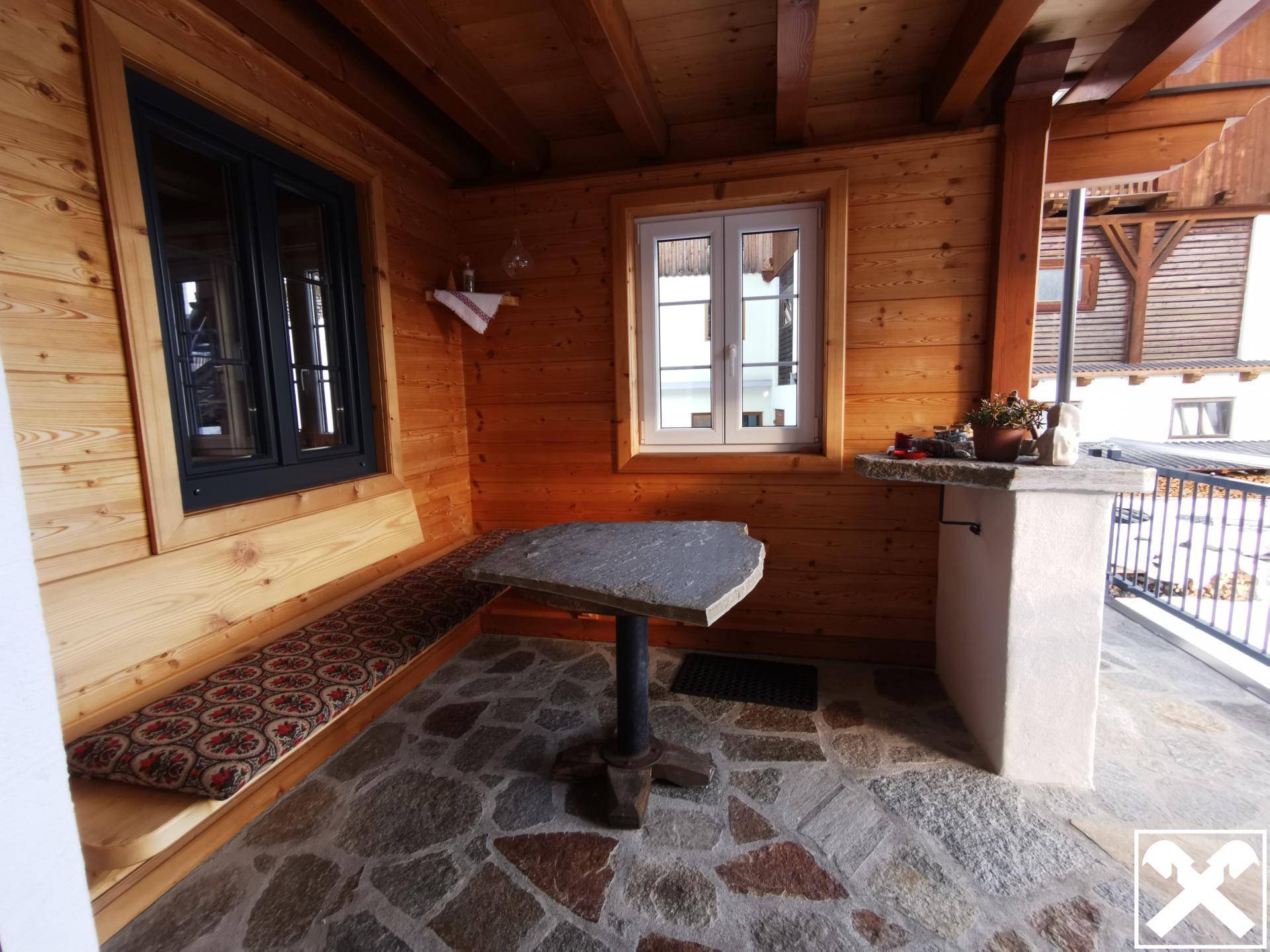 Überdachte Terrasse mit rustikalem Steinfußboden und gemütlicher Holzbank, ideal für entspannte Stunden.