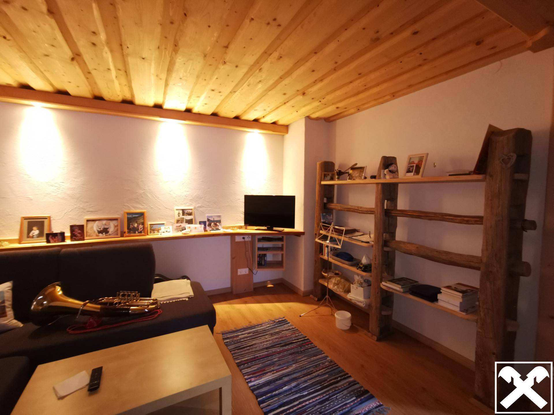 Gemütliches Wohnzimmer mit Holzbalkendecke, weiß verputzten Wänden und einem bequemen Sofa.