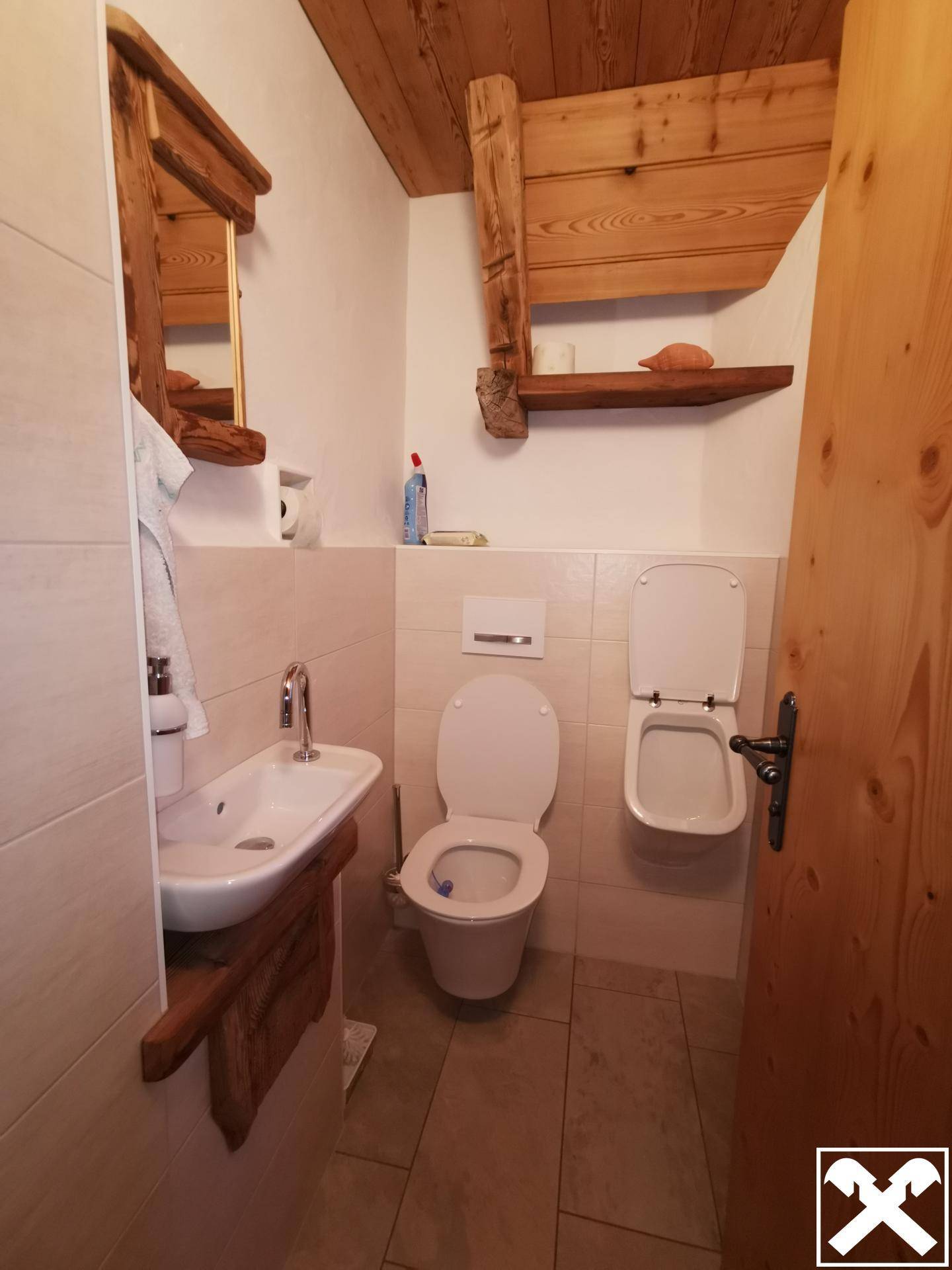 Separates WC mit Toilette, Bidet und kleinem Waschbecken, ergänzt durch rustikale Holzdetails.