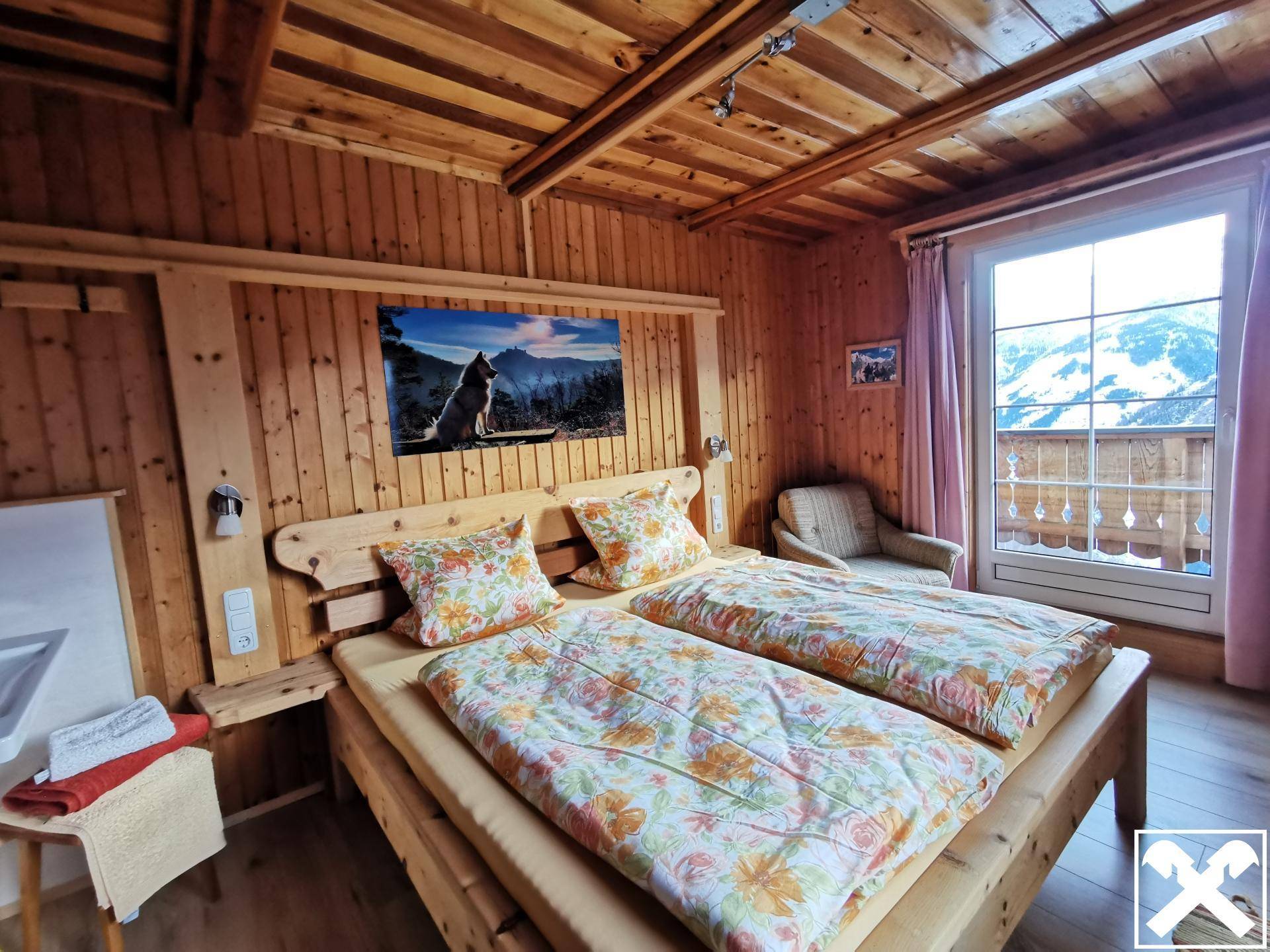 Gemütliches Schlafzimmer mit Doppelbett, Holzwänden und -decke sowie Zugang zu einem Balkon.