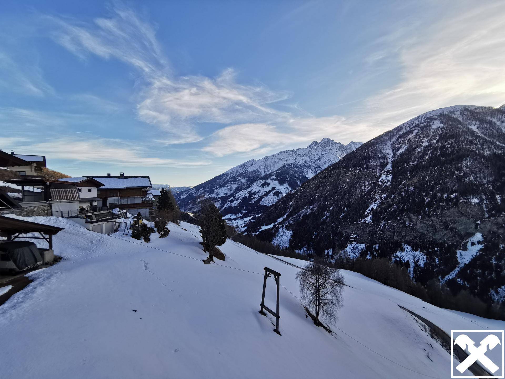 Weitläufige verschneite Berglandschaft mit einigen Häusern und einem klaren blauen Himmel.
