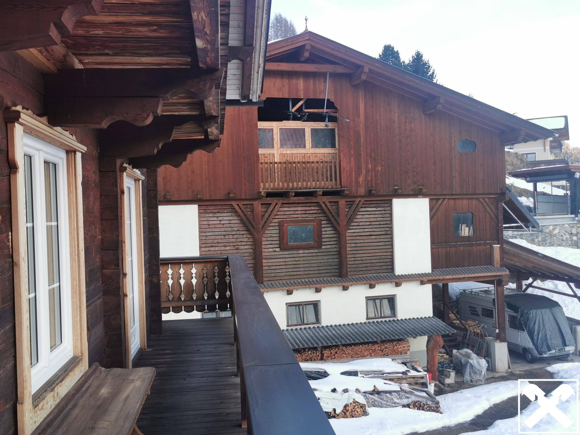 Balkon mit rustikalem Holzgeländer und Blick auf die umliegenden Gebäude und die verschneite Landschaft.