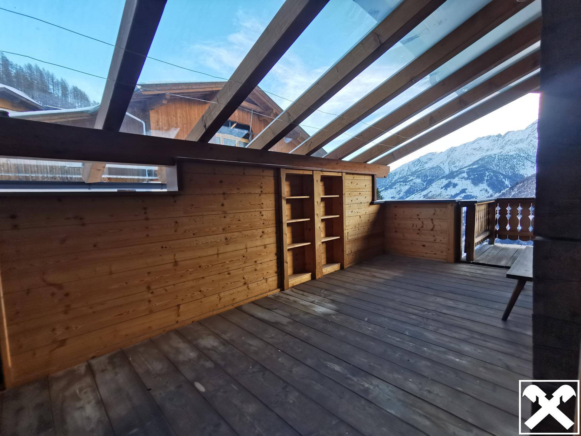 Geräumige Holzterrasse mit Glasdach und eingebauten Regalen, bietet einen weiten Bergblick.