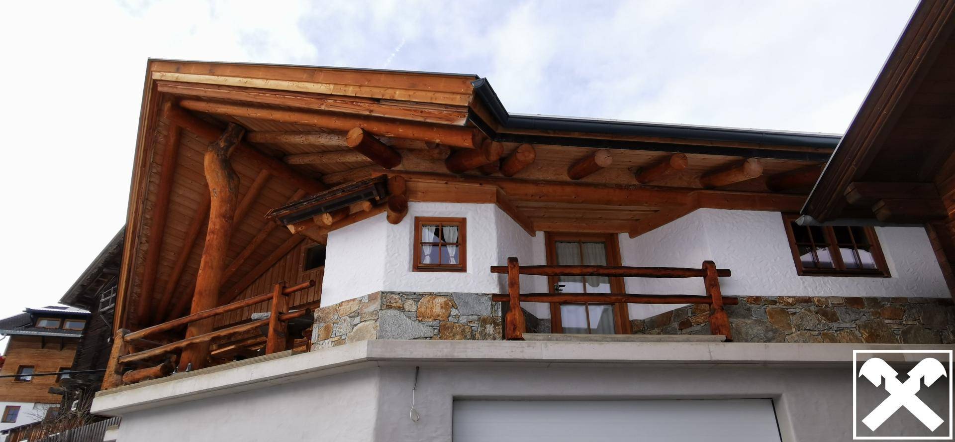 Gebäudeecke mit rustikalem Holzbalkon und dekorativen Steinelementen an der Fassade.