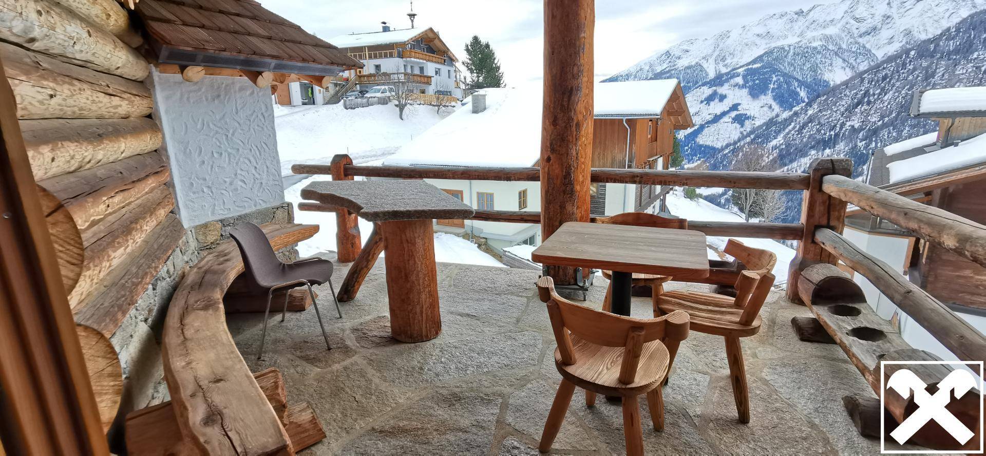 Gemütlicher Außenbereich auf einem Balkon mit rustikalen Holzmöbeln und beeindruckendem Bergblick.