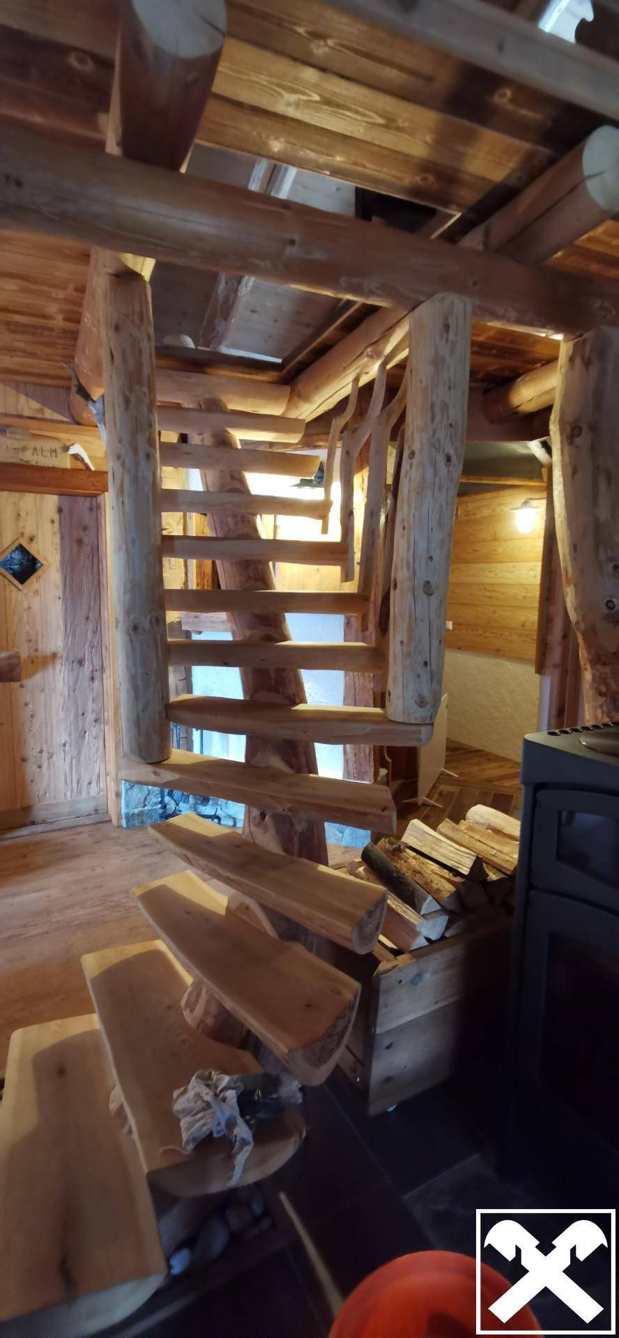 Rustikale Holztreppe führt in die oberen Stockwerke, mit Brennholz darunter gelagert.