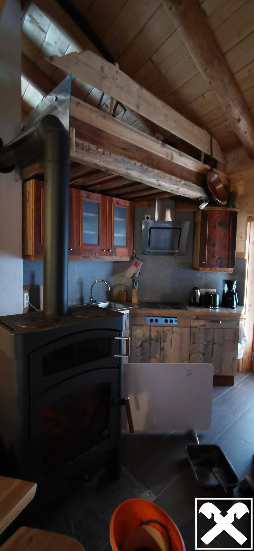 Rustikale Küche mit einem Holzofen im Vordergrund und Holzbalkendecke, strahlt Wärme aus.