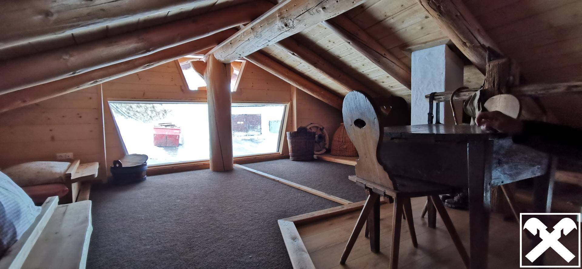Gemütlicher Dachbodenraum mit schrägen Holzdecken, Teppichboden und großen Fenstern mit Ausblick.