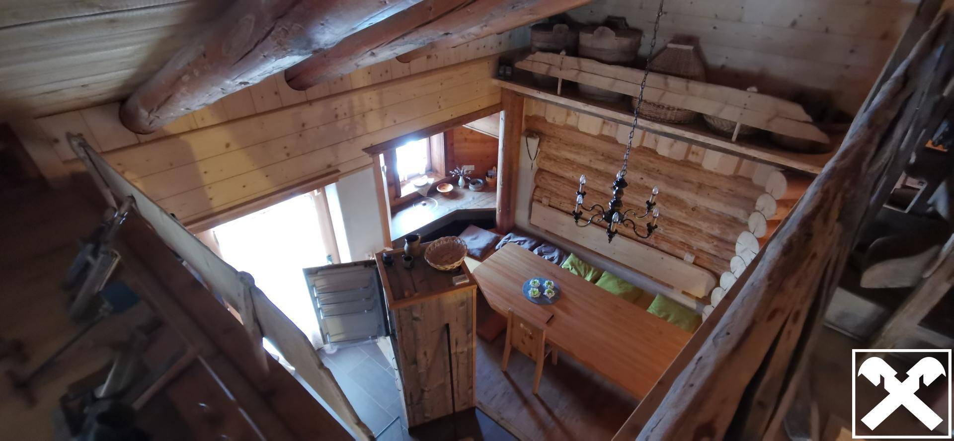 Blick von oben in einen rustikalen Essbereich mit Holztisch, Sitzbank und einem Kronleuchter.