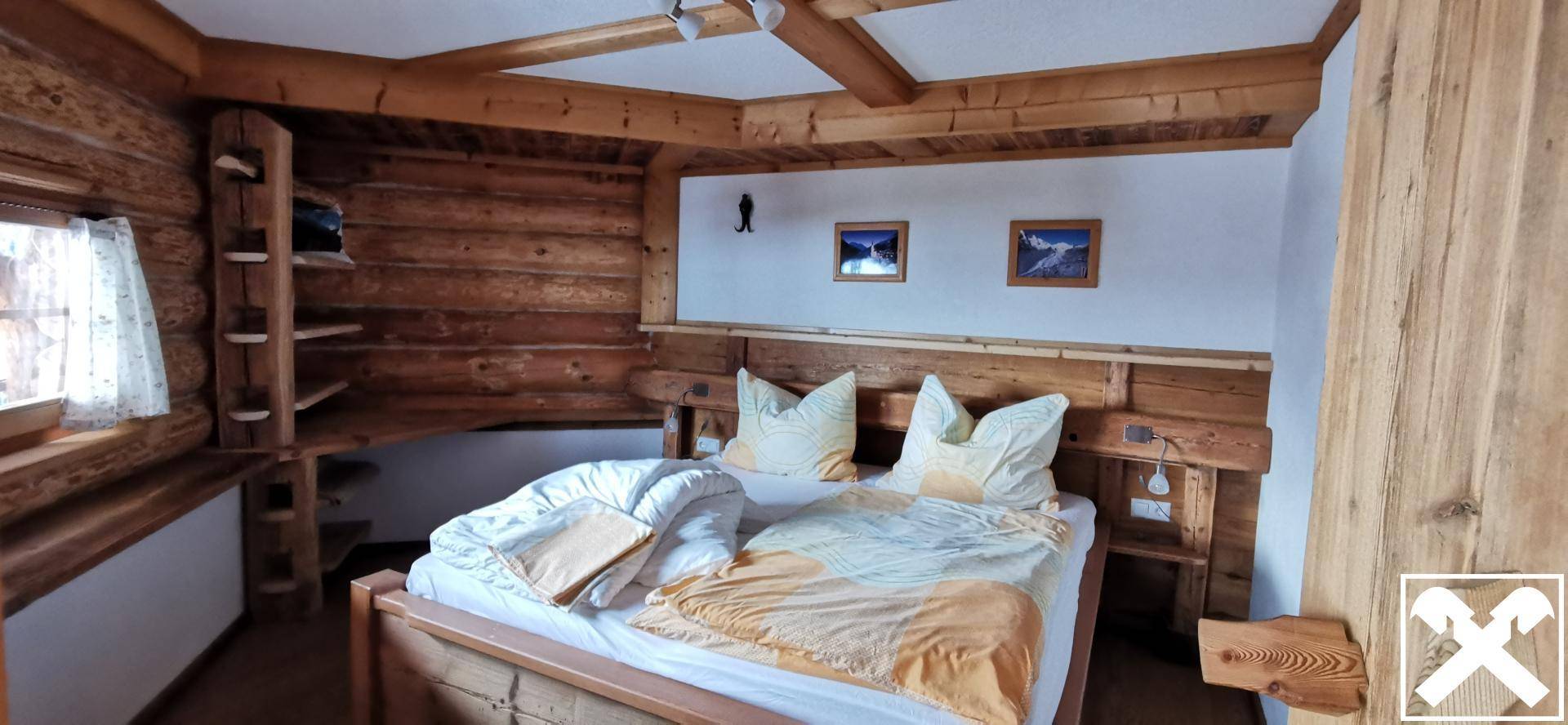 Gemütliches Schlafzimmer im alpinen Stil mit Holzbalken, Doppelbett und rustikaler Einrichtung.