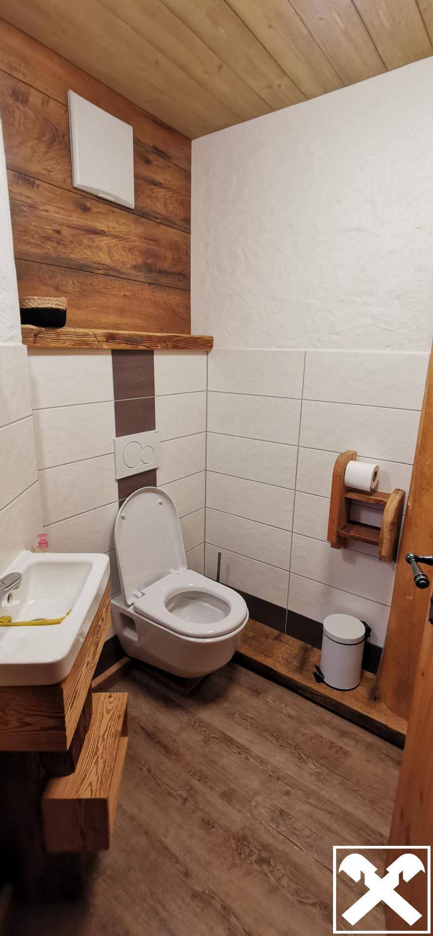 Modernes WC mit Holzverkleidung, weißen Fliesen und Laminatboden im alpinen Stil.
