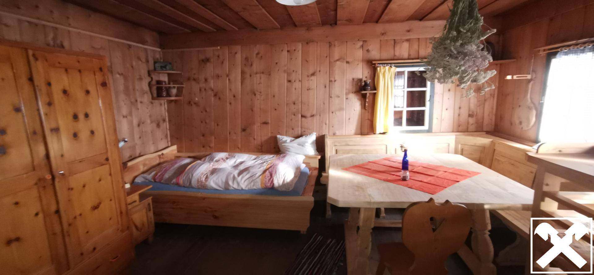 Helles, traditionelles Wohnzimmer im alpinen Stil mit Holztisch, Einzelbett und Holzwänden.