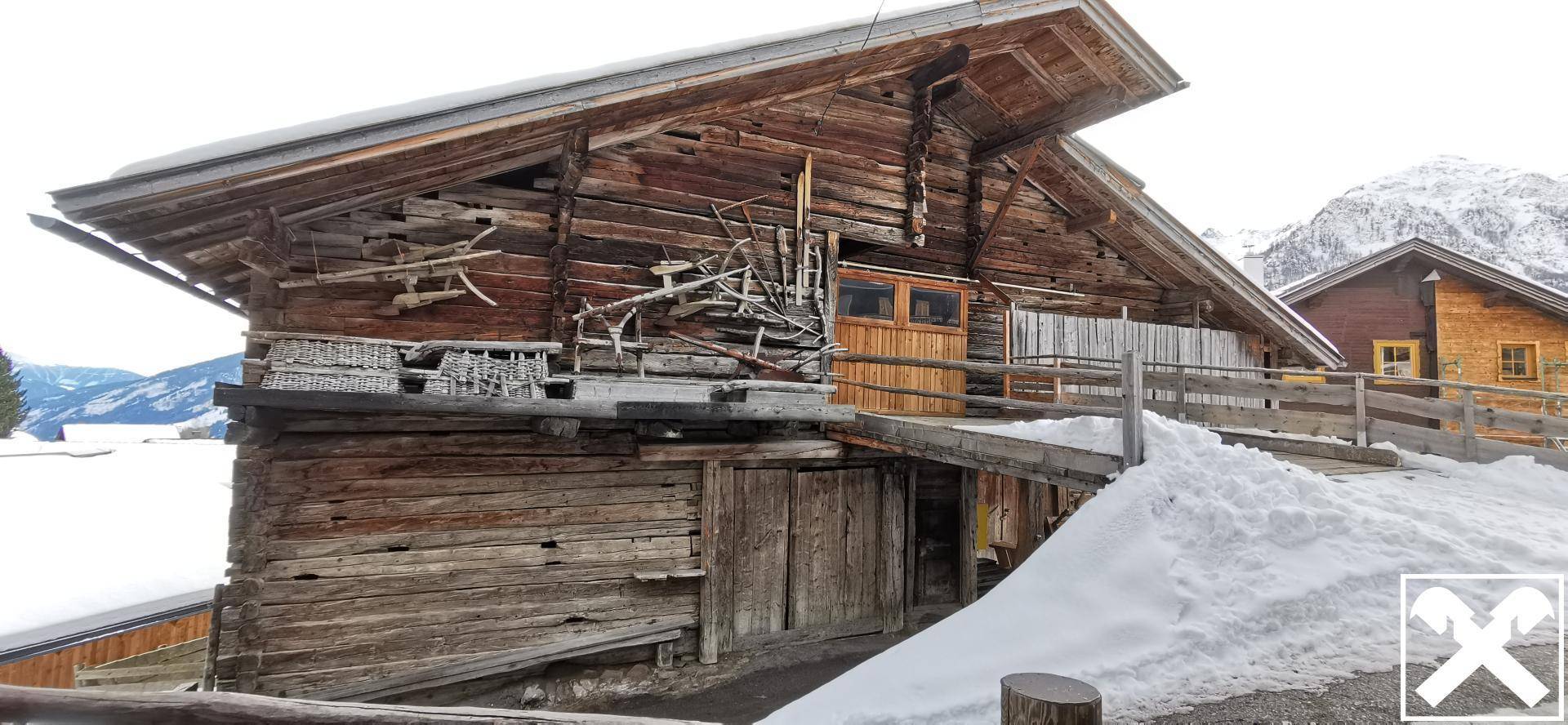 Altes Holzhaus mit rustikaler Fassade und verschneiter Umgebung, umgeben von Bergen.