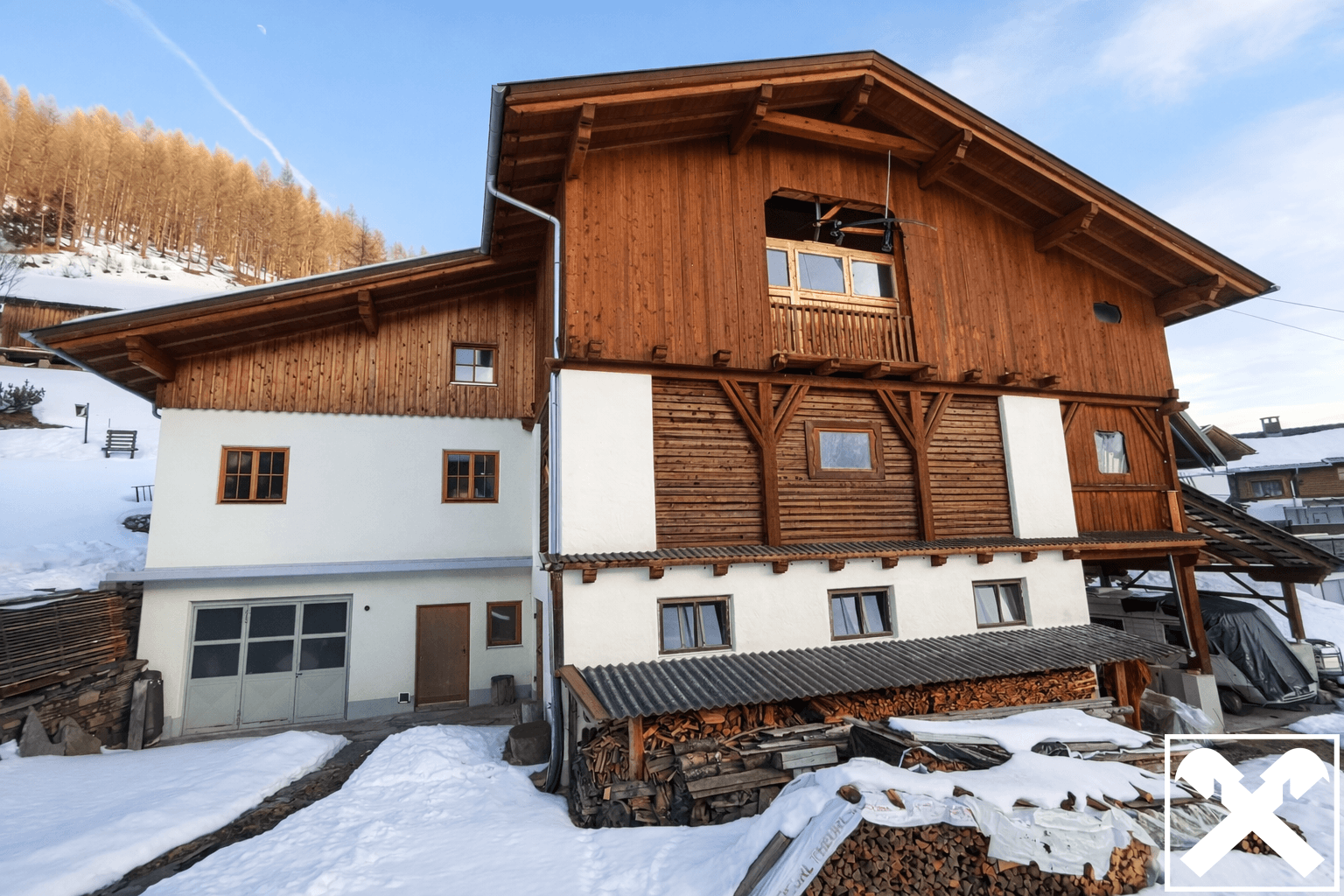 Großes Holzhaus im Chalet-Stil mit viel Holzfassade und gestapeltem Brennholz im verschneiten Gelände.