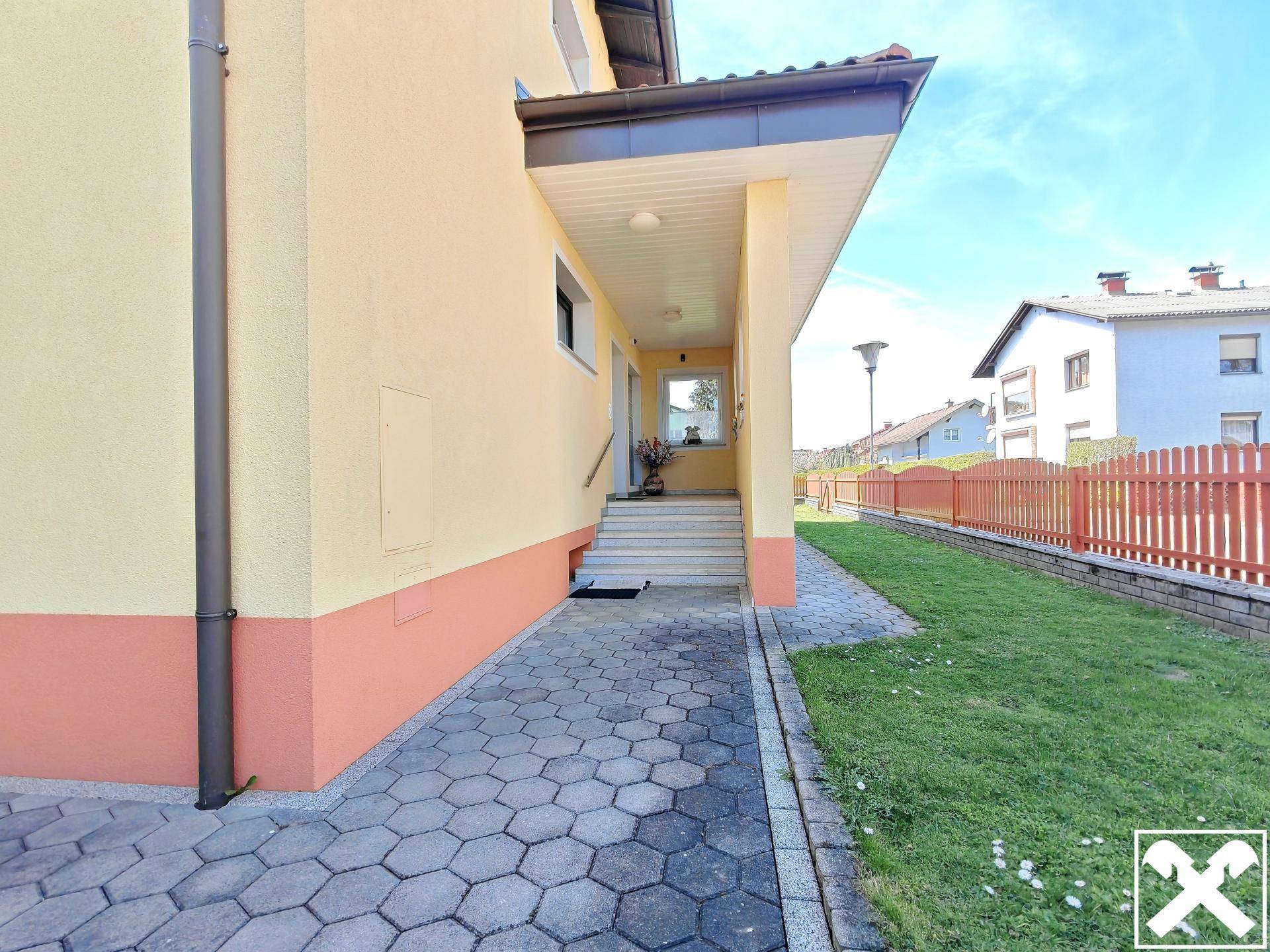 Überdachter Eingangsbereich des Hauses mit gepflastertem Weg und Vorgarten.
