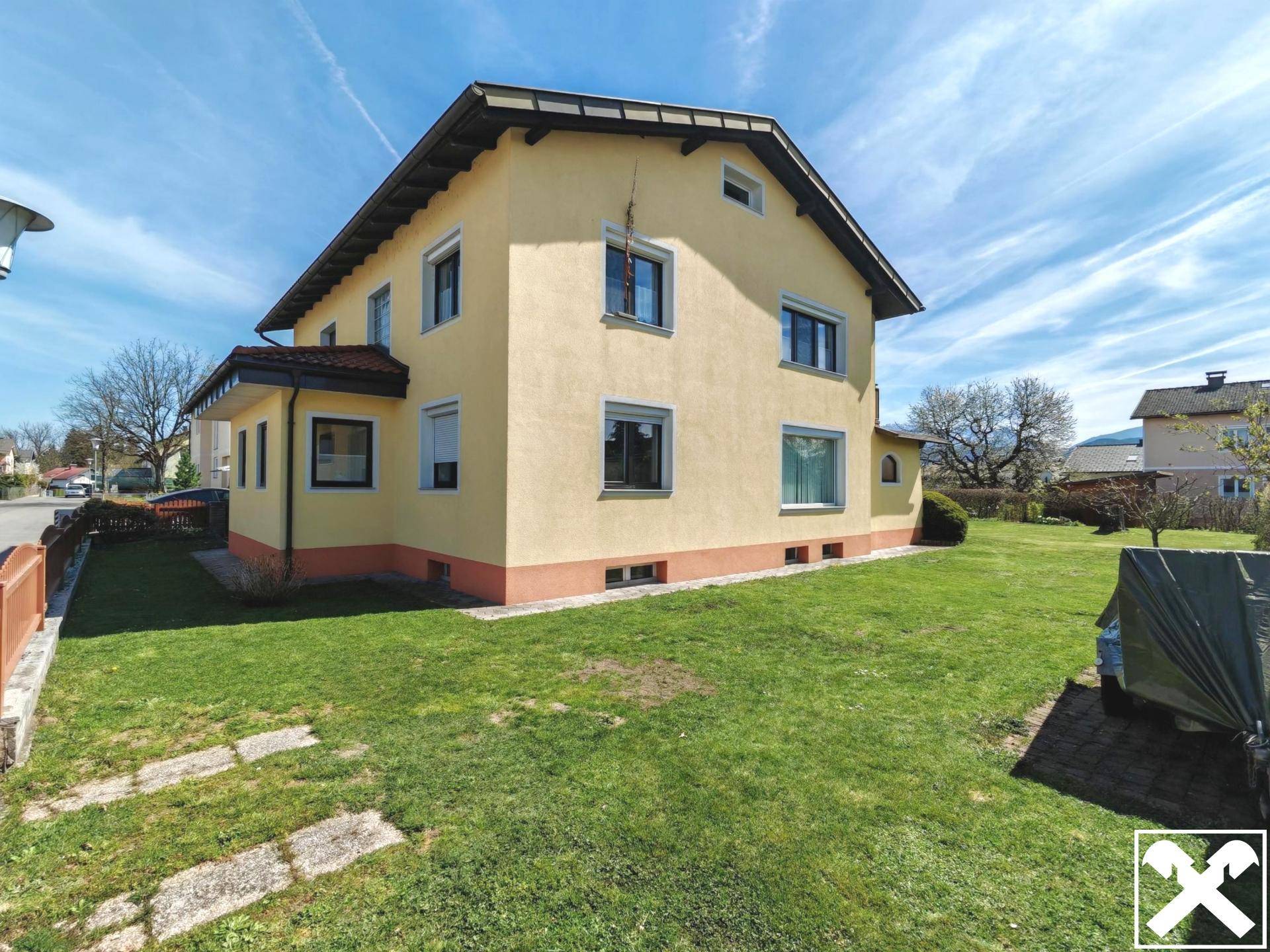 Seitenansicht des gelben Hauses mit gepflegtem Rasen und Fenstern zur Straße.