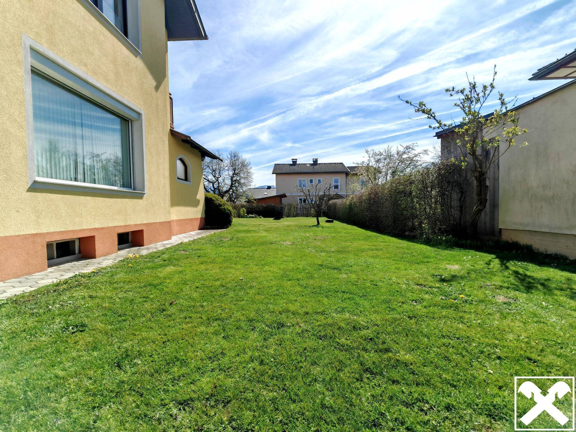 Seitlicher Rasenbereich des Grundstücks mit Hecke und Blick auf Nachbarhäuser.