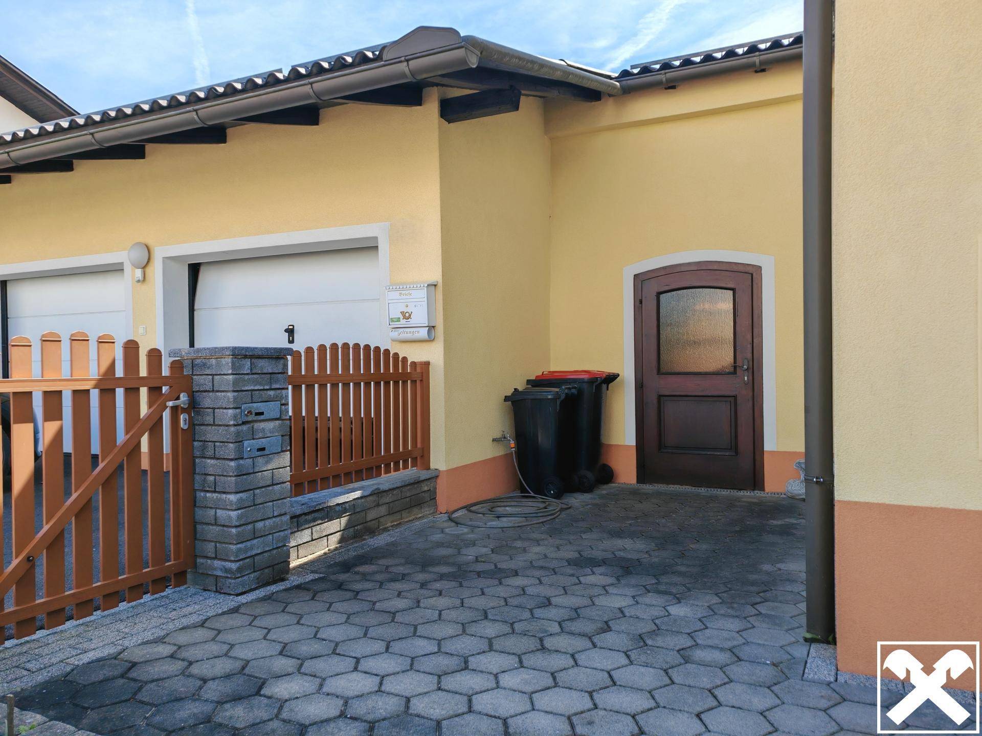 Eingangsbereich mit gepflasterter Zufahrt, Holzzaun und Zugang zur Garage.