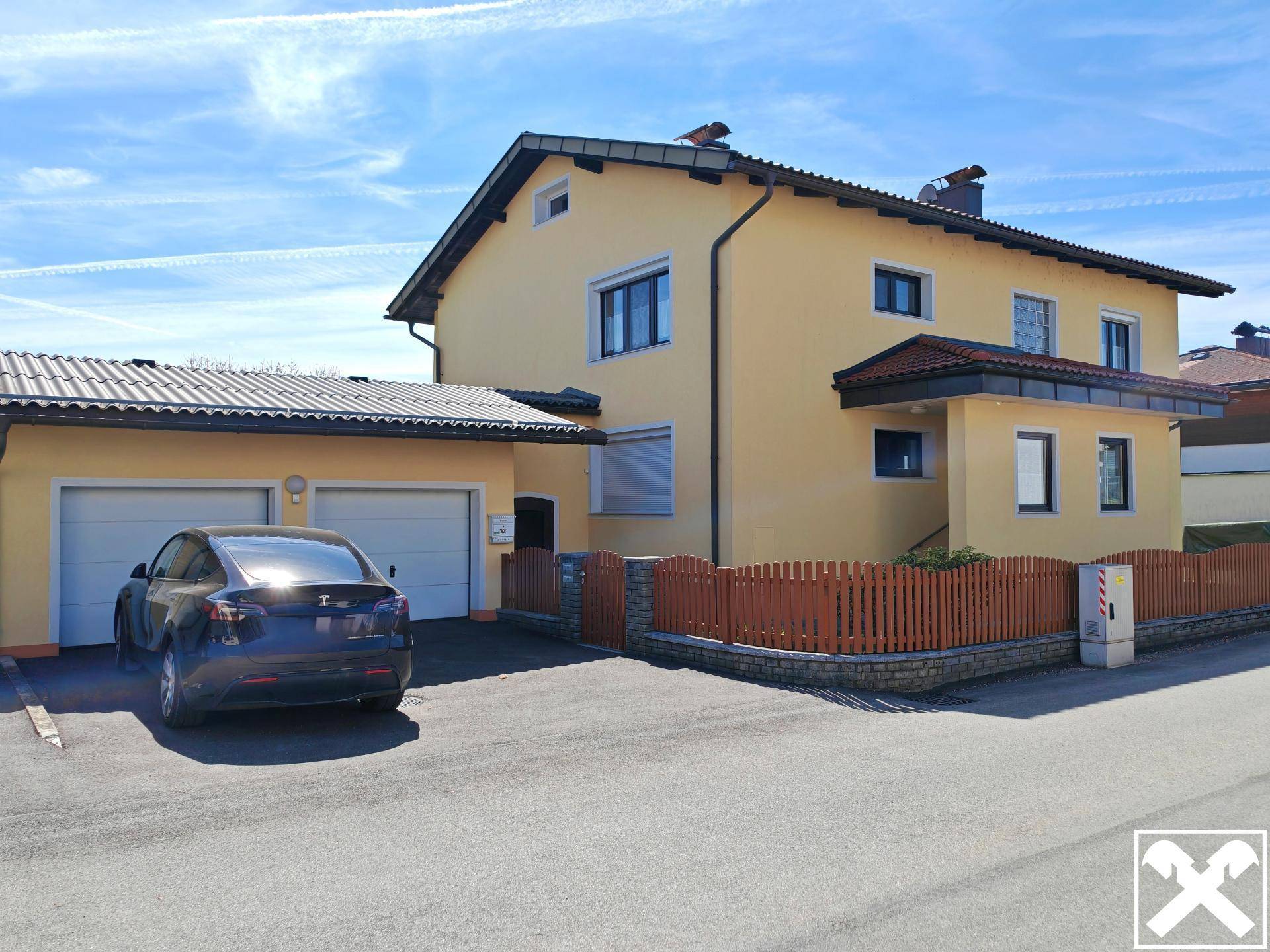 Vorderansicht des Hauses mit Doppelgarage, gepflasterter Einfahrt und Holzzaun.